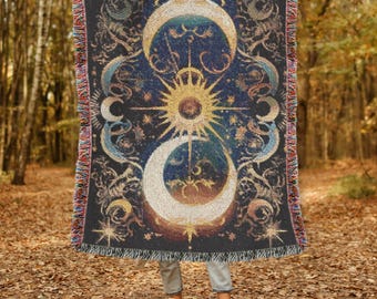 May include: A dark blue woven throw blanket featuring a celestial design with a sun, moons, and stars. The blanket has a fringed edge with a mix of colors. The design is in shades of gold, blue, and cream.