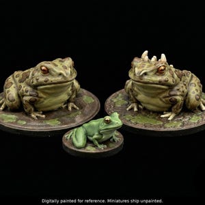 May include: Three frog figurines. Two larger frogs with textured green and brown skin sit on lily pads. A smaller, bright green frog is in front. The frogs have orange eyes and are set against a black background.