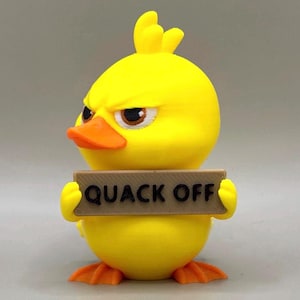 May include: A bright yellow duck figurine with an angry facial expression, featuring an orange beak and feet. The duck holds a rectangular tan sign in its wings with the black text QUACK OFF printed clearly across the front surface of the sign.