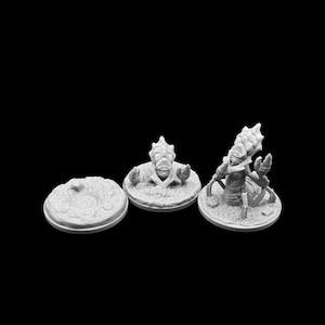 May include: Three gray miniature figurines of alien-like creatures. One is a circular base with a textured surface. The other two are on circular bases, one with a creature emerging and the other with a creature holding a tool.