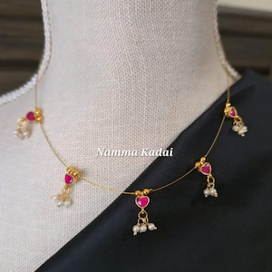 Puede incluir: Delicado collar de oro con colgantes rosas en forma de coraz&oacute;n y peque&ntilde;os grupos de perlas blancas. El collar se exhibe en un maniqu&iacute;, con el texto "Namma Kadai" visible.