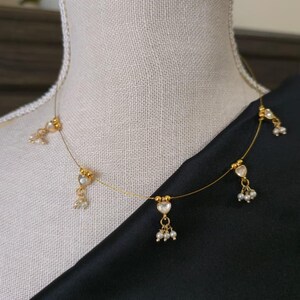 Puede incluir: Delicado collar de oro con colgantes en forma de coraz&oacute;n y peque&ntilde;os grupos de perlas. El collar se exhibe sobre un maniqu&iacute;, con una tela negra de fondo. Es una fina pieza de joyer&iacute;a.