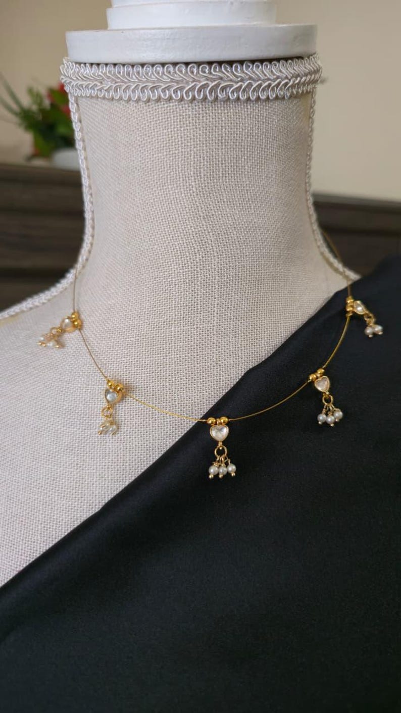 Puede incluir: Delicado collar de oro con colgantes en forma de coraz&oacute;n y peque&ntilde;os grupos de perlas. El collar se exhibe sobre un maniqu&iacute;, con una tela negra de fondo. Es una fina pieza de joyer&iacute;a.