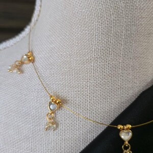 Puede incluir: Delicado collar dorado con colgantes en forma de coraz&oacute;n y peque&ntilde;os detalles de perlas. El collar se exhibe sobre un maniqu&iacute; con un fondo de tela de color neutro. El dise&ntilde;o es sencillo y elegante, adecuado para diversas ocasiones.