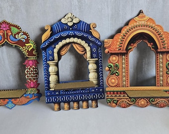 May include: Three decorative wall-mounted shelves shaped like arched windows. The left shelf features a brown frame with blue birds and pink lotus flowers. The center shelf is blue with yellow curtains. The right shelf is orange with floral patterns.
