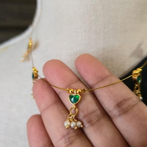Puede incluir: Delicado collar de oro con un colgante de piedra verde en forma de coraz&oacute;n y peque&ntilde;os detalles de perlas. El collar se exhibe en un maniqu&iacute;, mostrando su intrincado dise&ntilde;o. La joya es un hermoso accesorio.