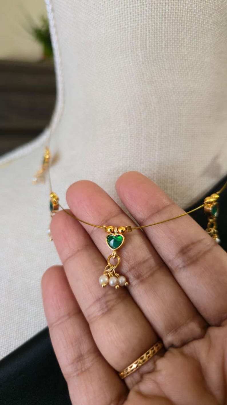 Puede incluir: Delicado collar de oro con un colgante de piedra verde en forma de coraz&oacute;n y peque&ntilde;os detalles de perlas. El collar se exhibe en un maniqu&iacute;, mostrando su intrincado dise&ntilde;o. La joya es un hermoso accesorio.