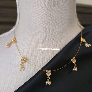 Puede incluir: Delicado collar dorado con colgantes en forma de coraz&oacute;n y peque&ntilde;os detalles de perlas. El collar se exhibe en un maniqu&iacute;, mostrando su dise&ntilde;o. El texto "Namma Kadai" es visible en la imagen.