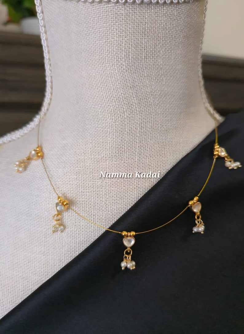 Puede incluir: Delicado collar dorado con colgantes en forma de coraz&oacute;n y peque&ntilde;os detalles de perlas. El collar se exhibe en un maniqu&iacute;, mostrando su dise&ntilde;o. El texto "Namma Kadai" es visible en la imagen.