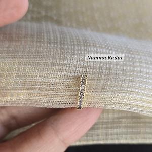 May include: A gold nose ring with a row of clear cubic zirconia stones. The ring is shown on a finger against a beige fabric background. The text "Namma Kadai" is visible in the image.