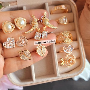 May include: A set of gold-tone jewelry in a jewelry box. The set includes a pair of pearl earrings, a pair of heart-shaped earrings, a pair of bird earrings, a ring with a heart design, and a ring with a rose design. The jewelry box has the text "COMBO BOX No: 1" on the top.