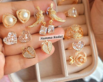 Puede incluir: Un conjunto de joyas doradas en una caja de joyería. El conjunto incluye un par de aretes de perlas, un par de aretes en forma de corazón, un par de aretes de pájaro, un anillo con un diseño de corazón y un anillo con un diseño de rosa. La caja de joyería tiene el texto "COMBO BOX No: 1" en la parte superior.
