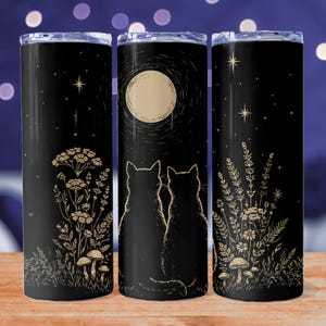 May include: Black stainless steel tumbler with a celestial design. The tumbler features illustrations of cats, a full moon, stars, and botanical elements. The design is in gold against a black background. The tumbler has a silver lid.
