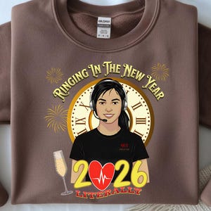 Puede incluir: Sudadera marrón con un gráfico que presenta a una mujer con auriculares, un reloj, fuegos artificiales y el texto "Ringing In The New Year". Debajo está "2026" con un corazón y la palabra "Literally". También se muestra una copa de champán.