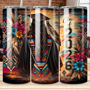 May include: A tumbler with a graduation theme, featuring a design with a graduate in a cap and gown, adorned with feathers and floral accents. The tumbler has the text "Class of 2026" and a colorful, southwestern-inspired pattern.