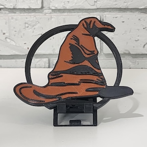 May include: A 3D printed figurine of the Sorting Hat from the Harry Potter series. The hat is brown and black and is sitting on a black stand.