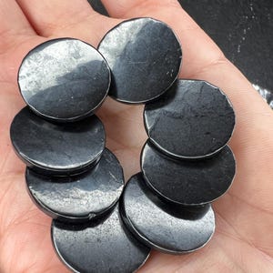 以下が含まれることがあります： 黒色の丸い滑らかな研磨された石が7つ集められています。石は円形に配置されており、中央に最も大きな石があります。