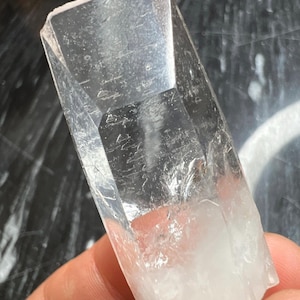 Puede incluir: Un cristal de cuarzo transparente con una punta puntiaguda y una base plana. El cristal es translúcido y tiene un ligero tono lechoso. Mide aproximadamente 12,7 cm de largo.