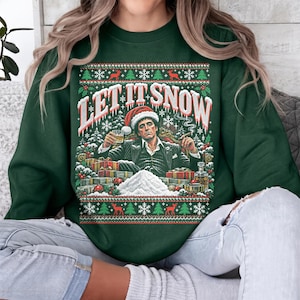 Puede incluir: Una sudadera de cuello redondo verde oscuro con un estampado gráfico de un hombre con traje y gorro de Papá Noel sosteniendo una bebida y un puro, con el texto LET IT SNOW, rodeado de árboles de Navidad, copos de nieve y regalos.