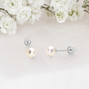 May include: A pair of silver stud earrings with small white pearl accents.
