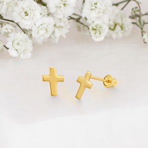 May include: A pair of gold cross stud earrings. The earrings are small and simple, with a smooth, polished finish.