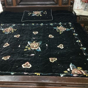 Puede incluir: Un edredón de terciopelo negro con intrincados bordados florales en hilo dorado, plateado y marrón. El edredón está acolchado y tiene un borde decorativo.