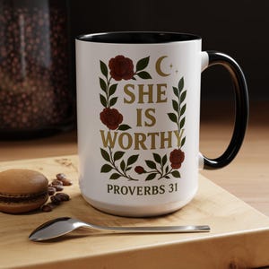May include: White ceramic mug with a black handle and interior. The mug features the text "SHE IS WORTHY" in gold, surrounded by red roses and green leaves. The words "PROVERBS 31" are printed at the bottom.