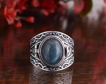 May include: Silver-toned ring featuring an oval, blue-green gemstone. The ring has an ornate, detailed design with a decorative border and side accents. The gemstone is set in a bezel setting.