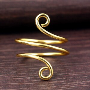 Peut inclure: Une bague en spirale de couleur or avec un design unique. La bague présente un fil continu et incurvé qui s'enroule autour du doigt, avec des volutes décoratives en haut et en bas. La bague est en métal brillant.