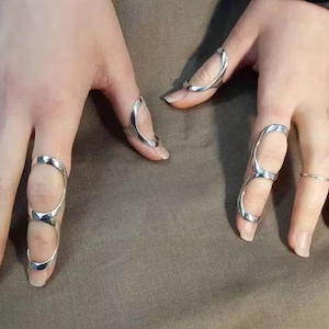 以下が含まれることがあります： さまざまなデザインのシルバーカラーの指輪。指先に巻き付くリングと、2つの関節を覆うオープンデザインのリングがあります。ニュートラルな背景にリングが表示されています。
