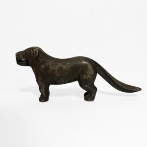 Peut inclure: Un casse-noix en forme de chien de couleur bronze. Le chien est en position debout, la gueule ouverte, révélant des dents. La queue est longue et incurvée. Le casse-noix est en métal et a une surface texturée.