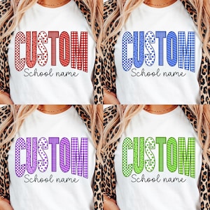 May include: A white t-shirt featuring the word CUSTOM in large block letters with varied patterns including leopard print, stars, stripes, and gingham, with the text School name underneath. Four color variations are shown: red, blue, purple, and green.