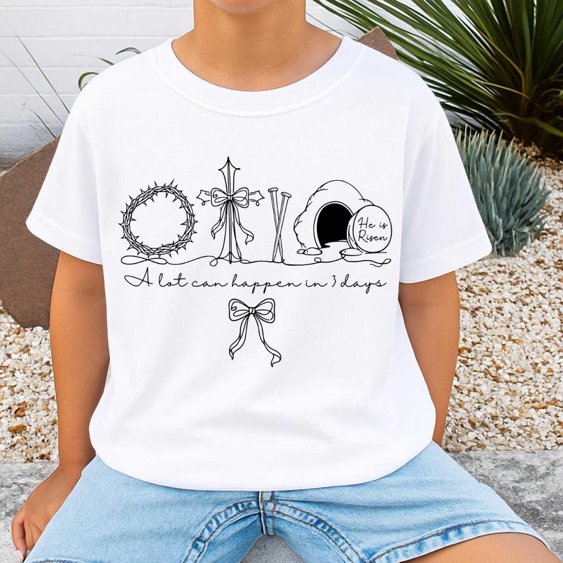 May include: White t-shirt featuring a black line drawing of Easter symbols: a crown of thorns, cross, nails, and an empty tomb with the text "He is Risen." The shirt also has the text "A lot can happen in 3 days."