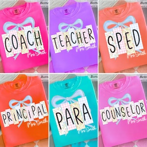 Puede incluir: Una colección de camisetas de cuello redondo coloridas. Cada camiseta presenta un diseño único con un lazo y las palabras "COACH", "TEACHER", "SPED", "PRINCIPAL", "PARA" y "COUNSELOR" en una fuente lúdica. Las camisetas son de varios colores, incluyendo rosa, morado, naranja y turquesa.