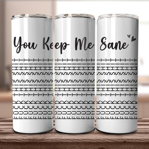 May include: Three white insulated tumblers with black text that reads "You Keep Me Sane". The tumblers have a repeating black pattern of dashes, squiggles, and curved lines. Two small black hearts are above the word "Sane".
