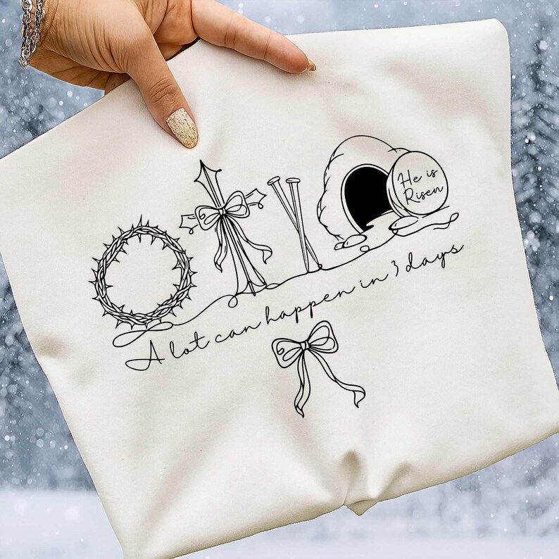 May include: Off-white tote bag featuring a black line drawing of a crown of thorns, a cross with a bow, nails, and an empty tomb with the words "He is Risen." The text "A lot can happen in 3 days" is also included.
