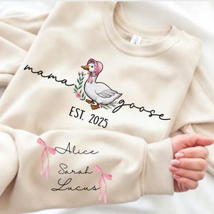 May include: A cream-colored sweatshirt with the text "mama goose est. 2025" and a cartoon goose wearing a pink bonnet. The sweatshirt also has the names "Alice", "Sarah", and "Lucas" written on it.