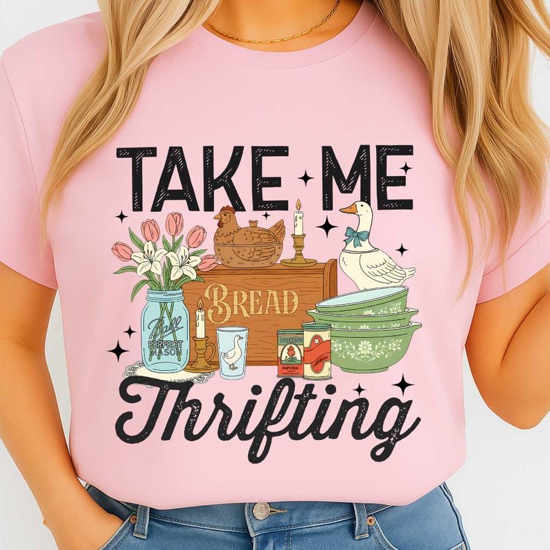 Puede incluir: Camiseta rosa con un dise&ntilde;o gr&aacute;fico que presenta el texto "TAKE ME THRIFTING". El dise&ntilde;o incluye ilustraciones de una gallina, un ganso, flores, un tarro de alba&ntilde;il, velas y utensilios de cocina vintage.