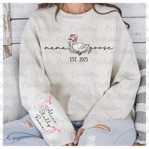 May include: A white sweatshirt with the text "mama goose est. 2025" and a cartoon goose wearing a pink bonnet. The left sleeve has the text "Alice Shelley Rose" with pink bows.