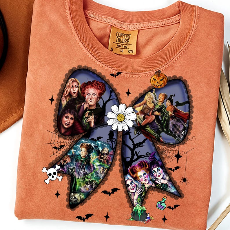 Op de afbeelding: Oranje sweatshirt met een groot strikdesign met afbeeldingen van heksen, een schedel, vleermuizen en een pompoen. De strik heeft een witte madelief in het midden. De sweatshirt heeft een ronde hals en lange mouwen. Het label zegt "COMFORT EBUDRIP".