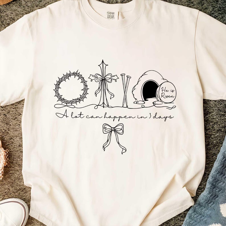 May include: Cream-colored t-shirt with a black line drawing of a crown of thorns, cross, nails, and an empty tomb with the words "He is Risen." The text "A lot can happen in 3 days" is also included.