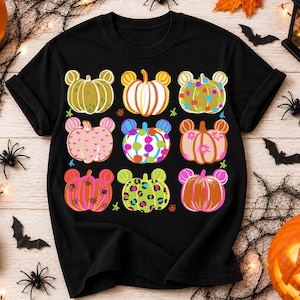 May include: A black short-sleeve t-shirt featuring a grid of nine colorful pumpkin illustrations. Each pumpkin has mouse-like ears and unique patterns including polka dots, hearts, leopard print, and stripes in various bright colors.
