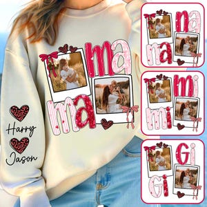 May include: Cream-colored sweatshirt with the word "Mama" in pink, featuring photo frames and heart accents. The left sleeve has the names "Harry" and "Jason" with heart designs. Additional designs include "Na", "Mi", and "Gi" with photo frames.