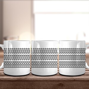 May include: Three white ceramic mugs with a black geometric pattern. The pattern consists of horizontal lines, zigzags, and other shapes. The mugs are sitting on a wooden surface.