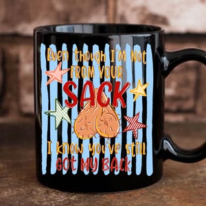 May include: Black ceramic mug with a humorous design. The mug features the text "Even though I'm Not From Your SACK, I know you've still GOT MY BACK" in red and white, with a graphic of testicles and star accents.