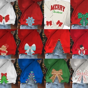 May include: A collection of 10 red, white, blue, and green sweatshirts with various Christmas-themed designs on the back. The designs include a bow, a snowflake, a Christmas tree, a gingerbread person, a snowman, and a light string.