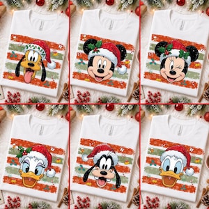 Puede incluir: Una colección de seis camisetas blancas, cada una con un personaje de Disney diferente usando un gorro de Papá Noel rojo. Los diseños incluyen a Pluto, Mickey Mouse, Minnie Mouse, Daisy Duck, Goofy y Donald Duck, sobre un fondo de rayas horizontales rojas y verdes con copos de nieve y acebo.