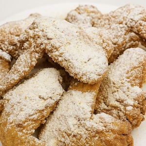 May include: A close-up shot of a plate piled high with golden-brown fried chicken wings, generously dusted with a white, powdery seasoning. The wings are crispy and appear freshly cooked, ready to eat.