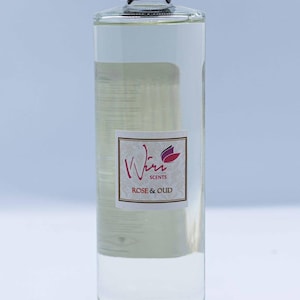 May include: A clear glass bottle with a black lid filled with a liquid. The bottle has a label with the text "Whim Scents" and "ROSE & OUD".