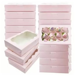 May include: A collection of light pink bakery boxes, some with clear windows. One box is open, revealing a view of the interior. Another box has a window displaying chocolate-covered strawberries with floral decorations. The boxes are stacked in neat rows.